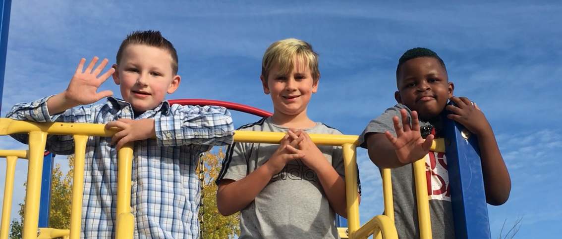 Three young boys on playground equipment and waving