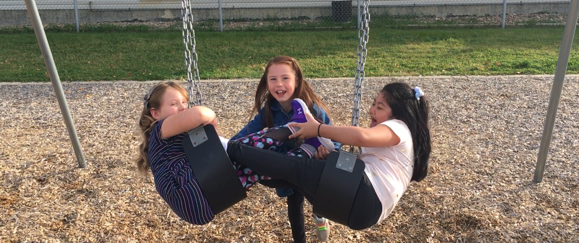 Three young girls playing on a swingset